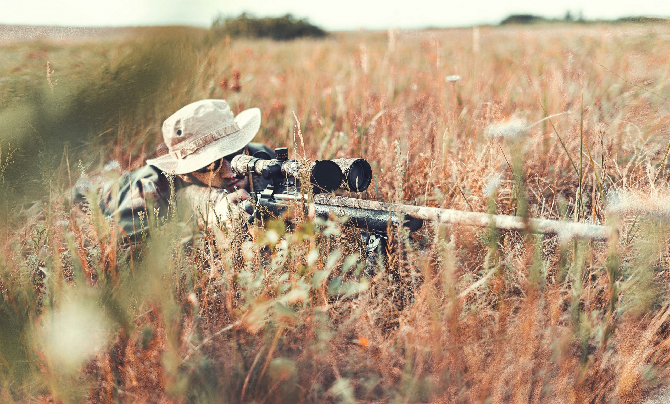 A hunter lies prone, aiming a scoped rifle, meticulously preparing for a Deer Hunt